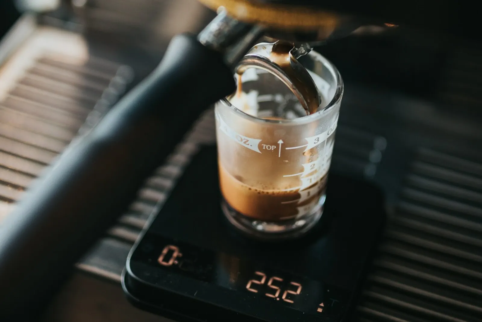 Espresso running into a glass shot cup on a small digital scale on a drip tray, the display reading 25.2