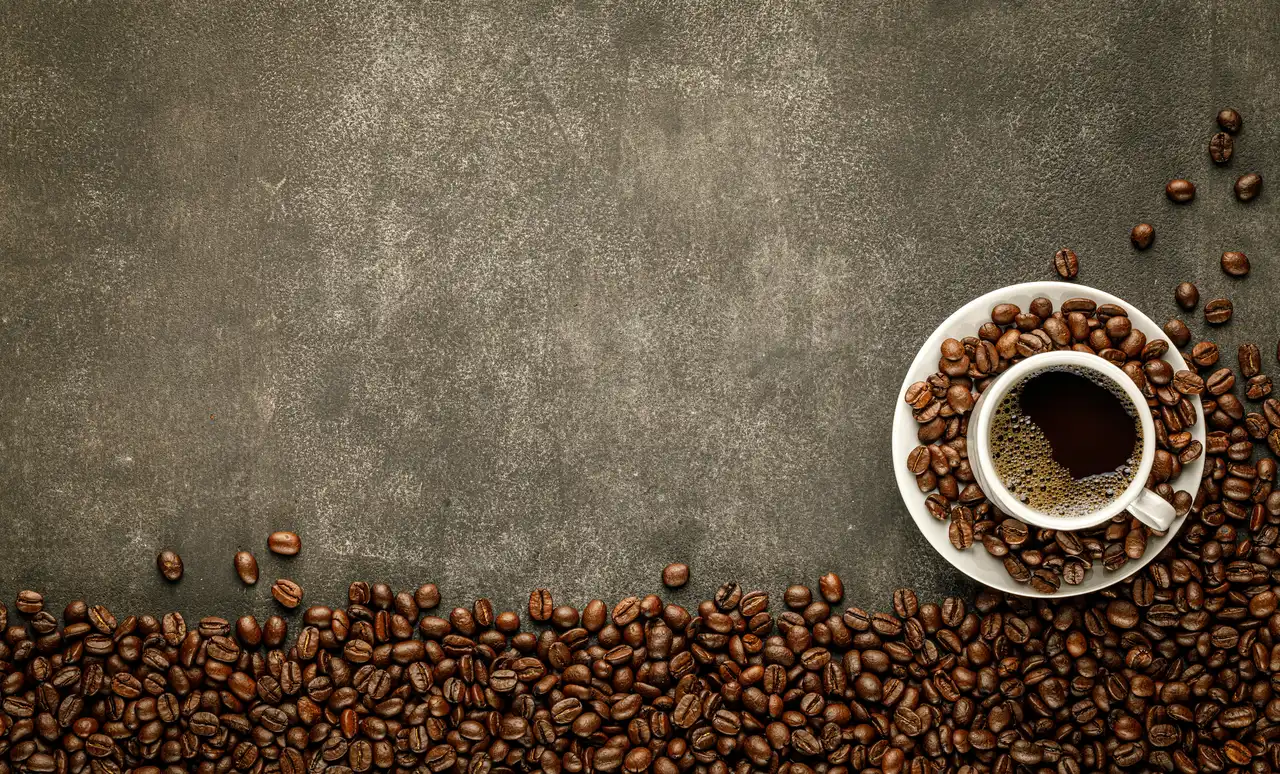 A cup of black coffee on a saucer of roasted beans, on a dark stone worktop